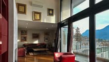 Spacious living room with large windows offering a scenic view, hardwood flooring, leather sofa and armchair, framed artwork on the walls, and air conditioning unit