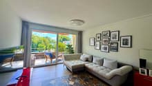 modern apartment living room, L-shaped couch, carpet, floor to ceiling windows, large balcony, trees view
