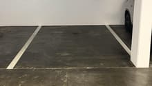 Underground parking lot with two parking spaces, white walls, grey floor, and white pillars