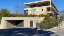 Modern architectural design, beige exterior, multiple levels, garage entrance, greenery on the roof, clear blue sky