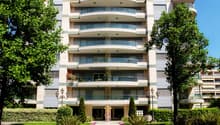 multi-story building, balconies on every floor, entrance with arch, multiple plants and trees