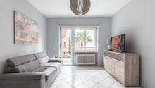 modern living room with gray couch, white tile floor, large windows, balcony, TV, wooden cabinet, radiator