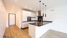 Empty modern kitchen with white cabinets, black countertops, wooden floor, oven, dishwasher, and sink with faucet.