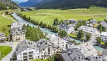 multi-story buildings, river, mountain landscape, surrounded by trees and greenery, flat roofs, gardens and driveways, yellow machinery in the river