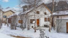 Snow-covered exterior, rustic design, wooden doors, snow-covered roofs, surrounded by trees, mountains in the background.