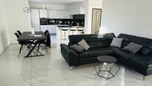 modern open plan living room, white marble flooring, sleek black leather sofa, modern dining table, white kitchen