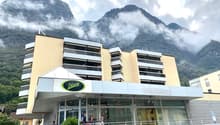 A multi-story commercial building with a parking lot in front, located in a mountainous area with clouds and fog in the background.
