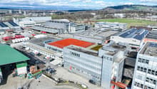 Industrial buildings with parking lots, solar panels on roofs, a red tennis court, multiple buildings, and surrounding area