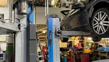 large metal rack system to lift cars, car in the middle, ladder against the wall, shelves with tools and equipment, car underneath a cover