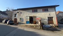 2 story house, concrete exterior, large windows, several cars parked in front, garage entrance, wooden posts, some clutter in the front