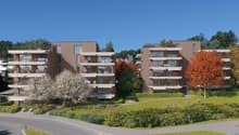 Multi-story apartment buildings with balconies, surrounded by landscaped gardens and trees. The buildings have a modern, minimalist design with clean lines and large windows.