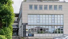 4-story commercial building with a glass facade, balconies on the top floor, and a parking area in front of the building