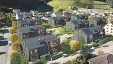Aerial view of a residential area with multi-story apartment buildings, surrounded by lush greenery and vineyards on the hills in the background.