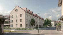 Apartment building, white exterior, brown roof, many windows, balcony on the first floor, streetlight, bushes, empty road