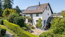 2 story house, brown roof, solar panels, white walls, surrounded by trees and shrubs, balcony