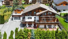 large chalet style house, wooden exterior, multiple balconies, parking area, garden