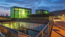 modern building with green glass walls, raised ground floor, metal railings, green roof