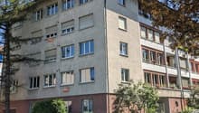 4 story building, multiple windows, red brick base, multiple balconies, trees, plants, car parked
