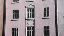 A multi-story pink building with several windows and a central entrance. The building appears to be an older, historic structure with a traditional architectural style.