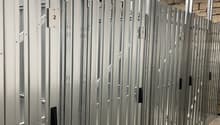 The image shows a row of gray metal storage lockers or compartments, likely in a storage facility or warehouse. The lockers have numbered doors and appear to be arranged in a long row with a high ceiling overhead.