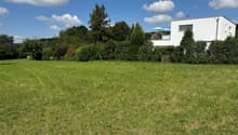 flat grassy field, modern white house, trees and bushes in background, clear blue sky