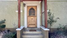 Wooden entrance door with glass windows, wooden pillars, stone stairs, plants