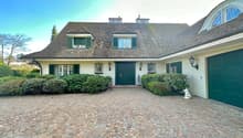 traditional style house, green front doors, brick driveway, green garage doors, lamps, bushes, statue, trees in the background