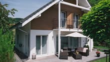 Detached house, 2 stories, brown and white, glass windows, wooden deck, chairs and table, umbrella, flower pots