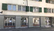 Storefront with green shutters, several windows, ground floor, two floors, sign on the left, three glass doors in front