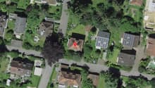 A neighborhood with residential houses surrounded by trees and grass. The houses are of different sizes and have brown roofs. Some houses have solar panels installed on their roofs. A few houses have driveways. In the center, there is a prominent house in