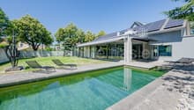 Modern house with solar panels, large windows, swimming pool, loungers, garden, trees