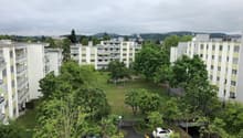 Aerial view of a residential building complex with multiple buildings, parking area, and a grassy field.