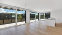 Spacious open-plan living area with large windows and sliding glass doors leading to a balcony, hardwood flooring, and a kitchen island.