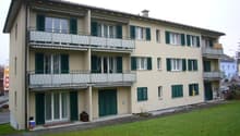 3 story apartment building, beige walls, green shutters, balcony on the top floor
