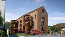 Modern apartment building with brick facade, wooden balconies, and a triangular roof design.