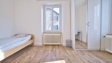 bed with blue blanket, radiator, trash bin, big mirror, window, wooden floor