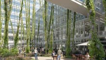 This image shows a large glass and steel commercial building with a lush, green indoor atrium. The atrium features hanging vines and plants, creating a natural and relaxing environment. There are people sitting at tables and chairs, suggesting this is a p