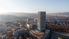 Aerial view of a city with a tall building, parking lot, and surrounding buildings