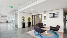 modern office lobby with glass walls, white walls, gray floor, two potted plants, three chairs, round table, carpet