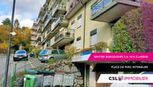 apartment building, multiple balconies, cars parked, trash bins