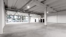 large open space with concrete floor, glass walls, exposed ceiling beams, visible parking area