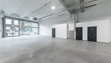 Empty parking garage, concrete flooring, white walls, double doors, and a large entrance