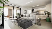Spacious open-plan living room with large windows, grey sofa, coffee table, and modern kitchen area with white cabinets and concrete countertops. The room has a minimalist and contemporary design with a balcony or terrace visible through the windows.