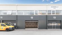 Commercial building with three garages, yellow van parked in front, large windows, gray exterior, number 11, 12, and 13 on the building