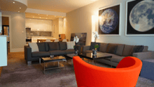 large living area with modern furnishings, 2 grey sofas, glass coffee tables, orange accent chair, large paintings on wall