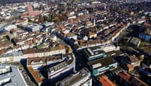 Aerial view of a densely populated city with many multi-story buildings, rooftops, and a mix of residential and commercial structures. The city appears to be a historic European urban center with a compact layout and narrow streets.