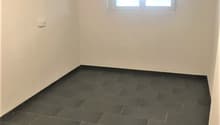 Empty room with white walls, grey tiled floor, one window.