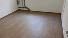 empty room, wooden floor, white walls, window with metal grill, pipes on the wall