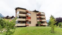 Apartment building with several floors, balconies, large front lawn, and potted plants on the balconies
