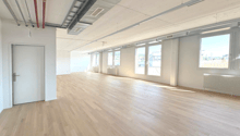 large room, hardwood floors, white walls, multiple windows, door at left, radiators